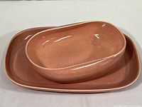 Pink sherbet oval serving bowl sitting inside rectangular platter showing color, shape, and scale