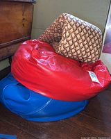 Image showing stacked red and blue round bean bag chairs with a woven bench cushion on top near wooden furniture.