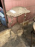 Full view of vintage brass plant stand showing detailed openwork design and curved legs, dusty and tarnished.