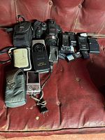 Panasonic DMC-FZ100 camera with Canon camera, camera cases, batteries, and chargers on a red leather surface.