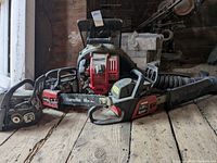 Photo showing two Poulan Pro chainsaws and one leaf blower on a wooden floor in a barn setting, all visibly dusty and used.