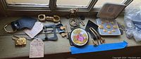 Overview of lot showing belt buckles, coin buttons, foreign coins in display box, decorative compact mirror.