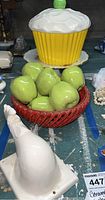 Various ceramic decorative and kitchenware items including white rooster figurine, green ceramic apples in red bowl, cupcake shaped cookie jar and Limoges cake stand