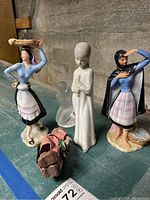Overview of all figurines on a blue surface with concrete wall background, showing the porcelain and frosted glass pieces together with the paper mache item.