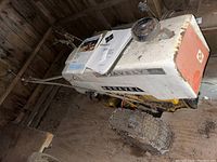 Side view of the Gravely push-behind tractor showing the white and orange body, one knobby tire, and a manual on top.