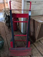 Front view of red and black metal hand truck/dolly showing frame, handles, and base plate
