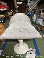 Side view of vintage footed milk glass centerpiece dish displaying scalloped edges and raised bead details around rim.