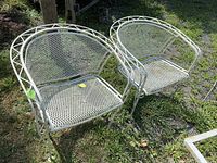 Pair of white wrought iron outdoor chairs on grass, showing front and side views with mesh seats and backs.