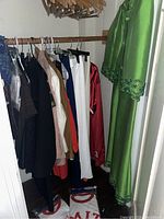 Wide view of assorted women's clothing items hanging on downtown and upper rods, including the green beaded gown set partially visible on the right side, and several other garments in black, red, tan, white, blue.
