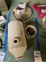 Photo showing bird planter hanger with metal hanging wires, stoneware hot water bottle, small bowl, and dish with decorative border on green surface