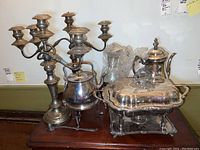 Photo showing the entire lot including candelabra, tea kettle, chafing dish, and candle snuffer on wooden surface.
