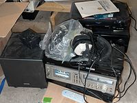 Full view of stereo equipment and speakers stacked including plastic bag with cables and Sylvania headphones on top.