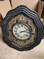 Front view of vintage wooden wall clock with scalloped black frame and decorative inlay surrounding clock face with Roman numerals.
