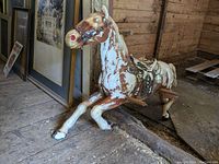 Side front view of vintage plastic rocking horse showing painted bridle detail, saddle, and wear on paint surface.