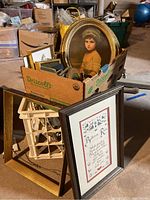 Wide view of the lot showing a Driscoll's blueberry box filled with framed art and empty frames, an oval framed portrait, and some empty frames against a crate.