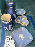 Five Wedgwood jasperware pieces including vase, pitcher, heart-shaped dish, round dish, and rectangular dish seen together on green surface.