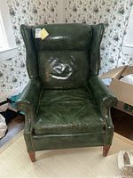 Front view showing green leather upholstery, wing back design, tacked edging, and wooden legs.