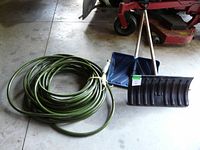 Photo showing the full coil of the 100 foot green garden hose alongside the two plastic snow shovels.