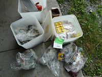 Three white plastic buckets filled with bags of assorted sewing buttons and notions on concrete floor