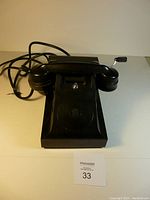 Front-facing view of black antique Bakelite telephone with handset and visible crank handle on the right.