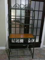 Front view of green metal baker's rack with wood shelf and metal scrollwork design