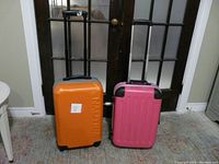 Front view of Nautica orange and grey suitcase and United Colors of Benetton bright pink suitcase side by side with handles extended.