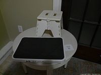 Photo of white plastic folding stool and metal folding stool placed on round white table near window