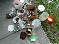 Overview of all containers and bags filled with buttons on a concrete surface outdoors.