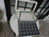 Top view of white wood jewelry display case with glass lid showing four large compartments, placed on a round white table.