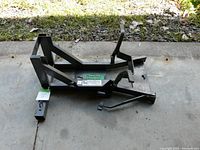 Side angle view of the black metal motorcycle wheel lock showing angled braces and foot pedal lever, placed on concrete floor.