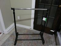 Full view of adjustable height clothes rack showing metal frame, plastic parts, base with wheels, and horizontal hanging bar.