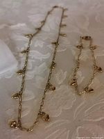 Full view of necklace and bracelet laid out on fabric, showing gold plated chains with small puffy heart charms, alongside the white velvet bag.