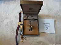 Three ladies watches displayed: Seiko wristwatch with gold case and brown leather band, vintage Pulsar black dial wristwatch, and Pulsar quartz watch necklace in box.