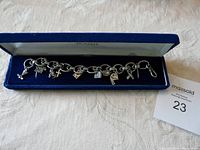 Sterling silver link charm bracelet with 9 distinct silver charms, displayed in an open blue velvet box on a fabric surface.