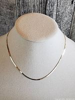 Front view of the sterling silver herringbone chain necklace displayed on a fabric bust, showing the chain's flat and shiny design.