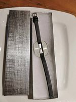 Single watch in black leather strap inside textured gray box with white padding.
