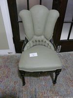 Front angle view of the vintage parlor chair showing button tufted high back and painted sage green fabric upholstery along with the black painted wooden frame and legs with caster wheels.