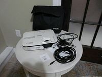 Epson EX3210 projector on white small round table with power and VGA cables coiled next to it and black carrying case behind it