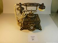 Front view of ornate metal and plastic reproduction rotary dial telephone with handset and coiled cord, showing overall design and size.