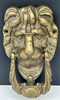 Full view of antique brass lion head door knocker, showing overall shape and ring handle attached to mouth.