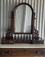 Close view of arched mirror held by carved wooden supports atop three small top drawers resting on marble slab