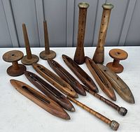 Photo showing 15 antique wooden weaving tools including shuttles and spools on a white surface outside.