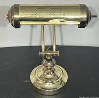 Front view of the vintage brass bankers lamp showing the polished brass cylindrical shade with diamond-shaped perforations and the weighted round base.