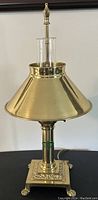 Full view of vintage brass desk lamp with polished conical shade and clawfoot square base.
