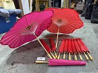 Photo showing 12 decorative umbrellas arranged on a floor, 10 red and 2 pink, 2 opened for display and 10 closed.