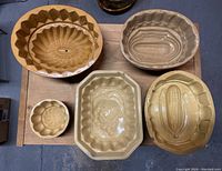 Five pottery molding forms shown from a top-down angle on a wooden surface, displaying varying designs such as corn cob and floral.
