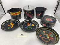 Full view of all hand painted tins, pails, plates, and round box arranged on white surface.