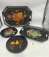 Front view of all four trays showing painted floral and fruit designs on black background, two rectangular and two round.