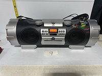 Front view of JVC boombox showing speakers, controls, and display lit up tuning to FM 107.9.