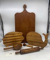 Overall front view of the wooden cutting boards, scoop, rolling pin and small hand tool displayed together on a white surface.